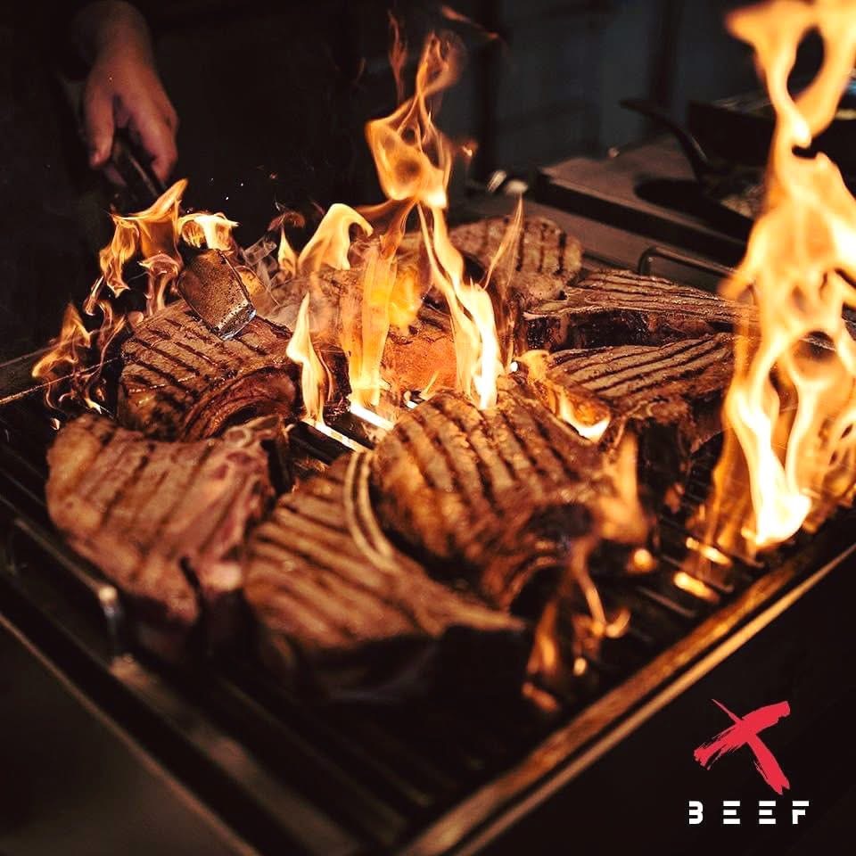 X BEEF steaks grilling over flame